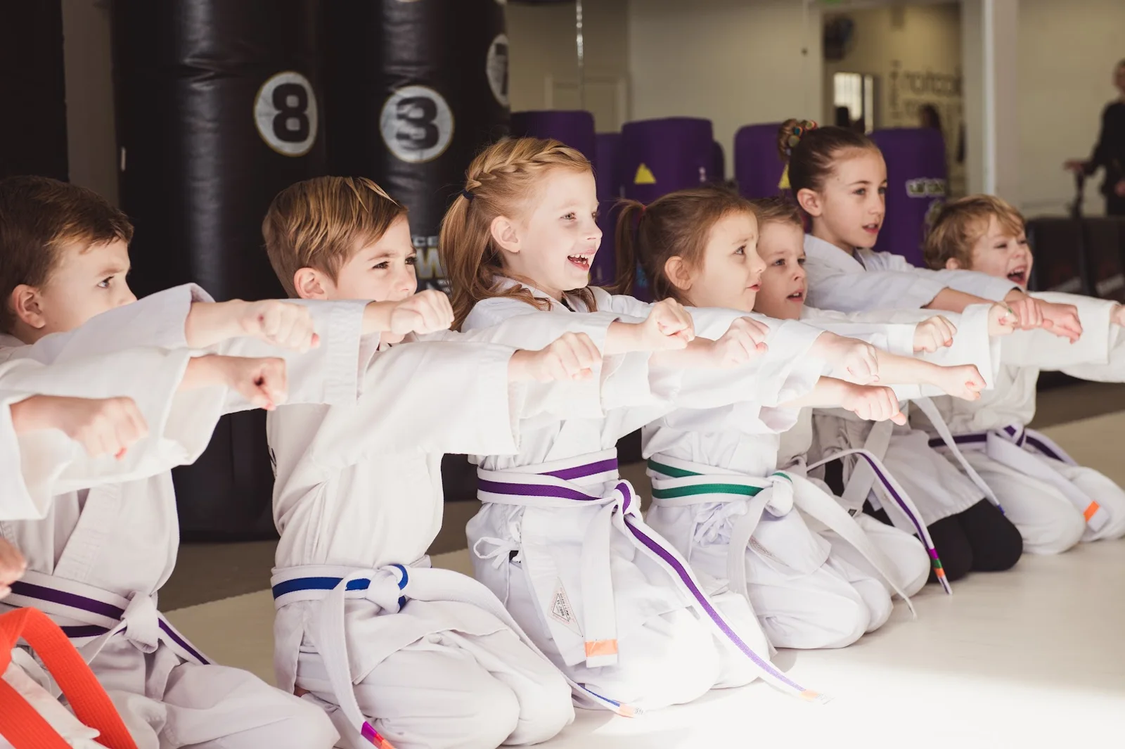 An instructor closely supervising preschool students on the mat